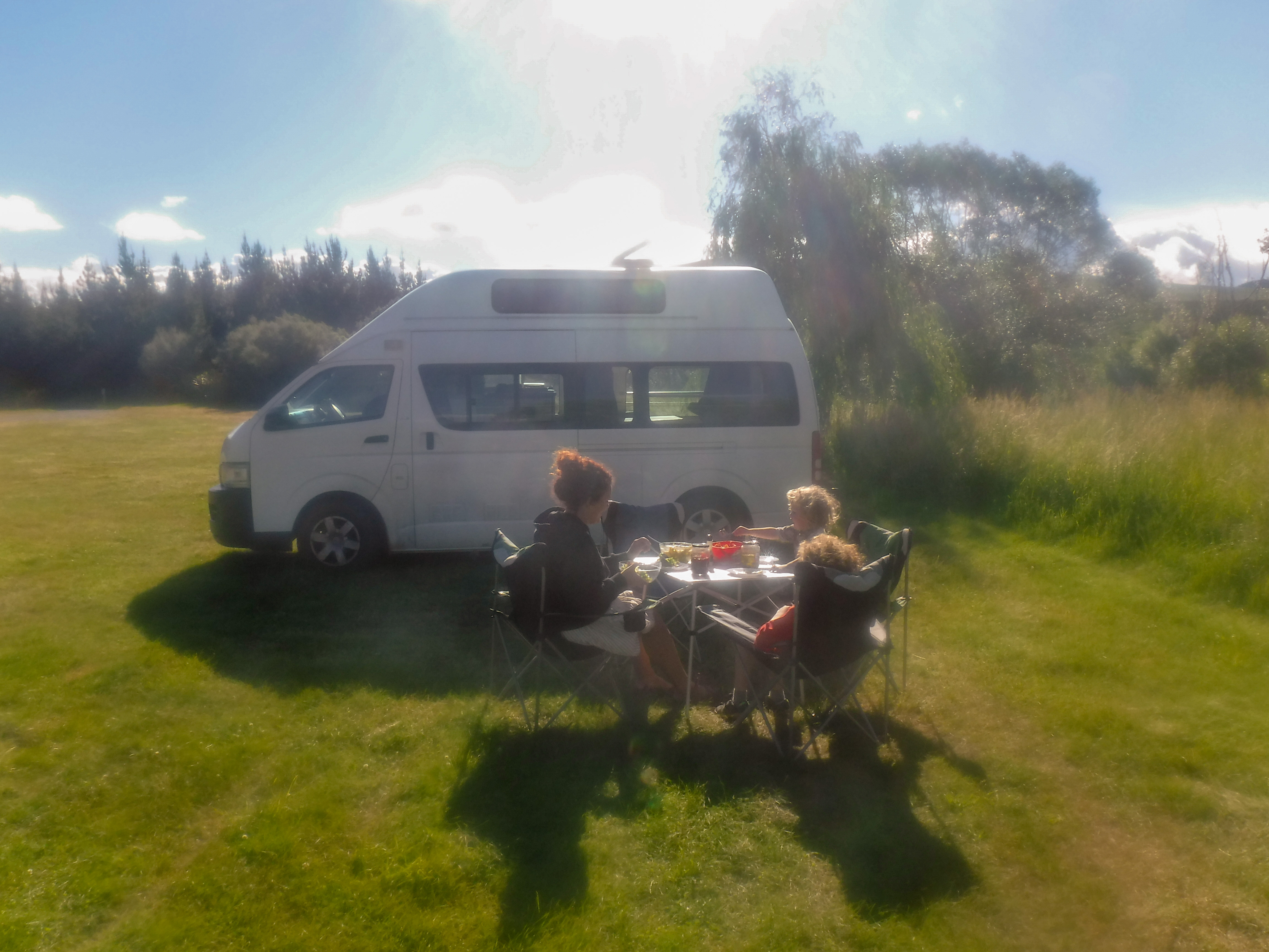 Family Sat Around Table next to Campervan in field in New Zealand