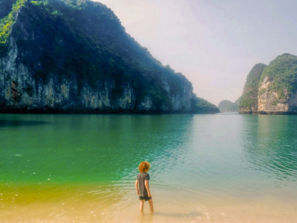 child stood in water in front of limestone rocks at Ha Long Bay in Vietnam