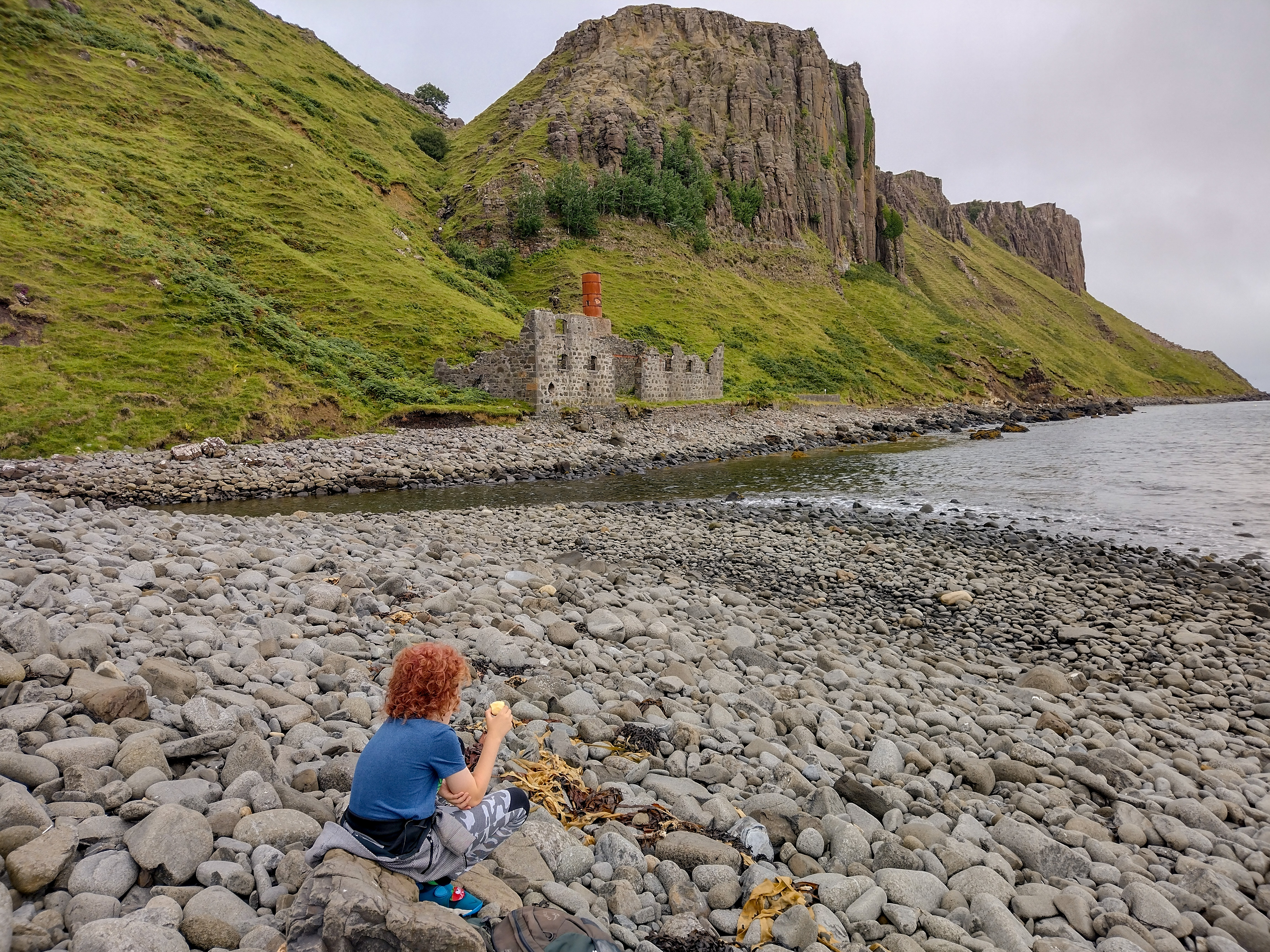 Child sat on the shore near Lealt Falls in Scotland