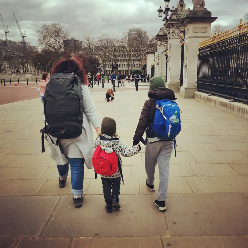 Family walking past Buckingham Palace with backpacks in London